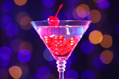 Photo of Cocktail with casino dice in glass against blurred lights, closeup