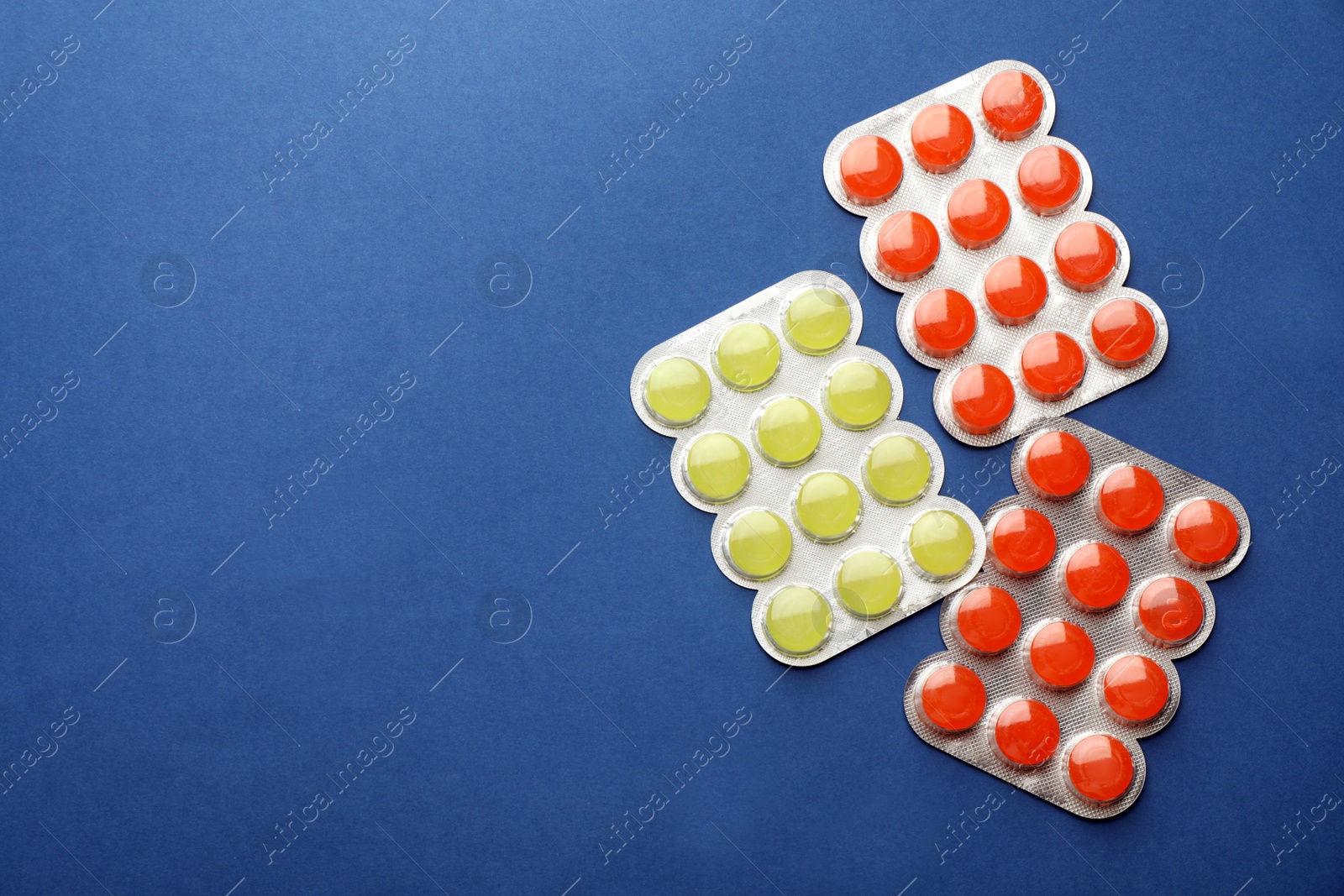Photo of Blisters with colorful cough drops on blue background, flat lay. Space for text