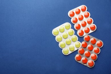 Blisters with colorful cough drops on blue background, flat lay. Space for text