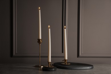 Elegant candlesticks with burning candles on grey table