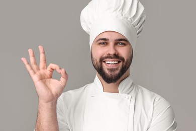 Happy young chef in uniform showing ok gesture on grey background