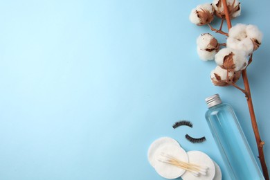 Bottle of makeup remover, cotton flowers, pads, swabs and false eyelashes on light blue background, flat lay. Space for text