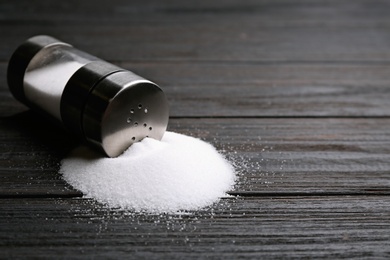 Photo of Scattered salt and shaker on black wooden table, closeup. Space for text