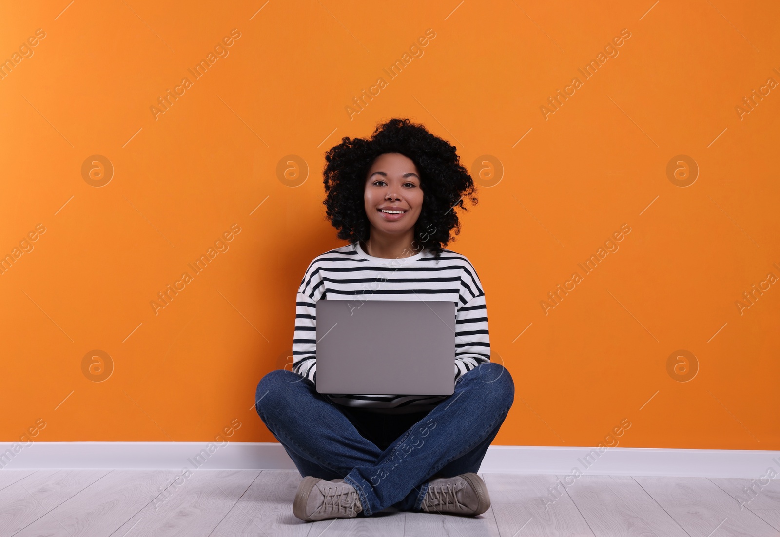 Photo of Happy young woman with laptop sitting near orange wall