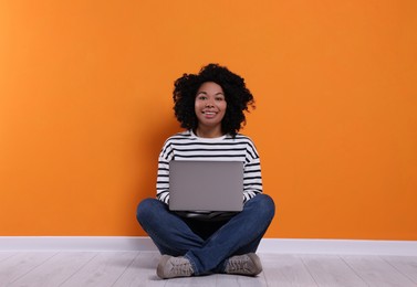 Happy young woman with laptop sitting near orange wall