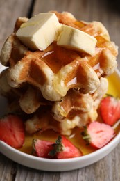Photo of Delicious Belgian waffles with honey, butter and strawberries on wooden table, closeup