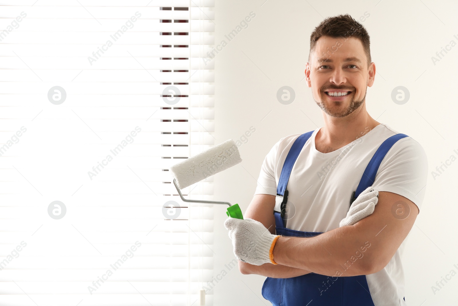 Photo of Man holding paint roller near window indoors. Space for text