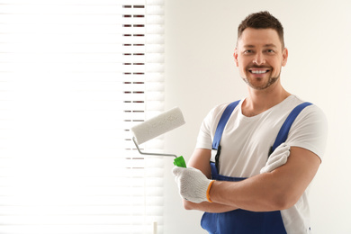 Photo of Man holding paint roller near window indoors. Space for text