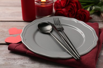 Romantic place setting with red roses, candle and decorative hearts on wooden table. St. Valentine's day dinner