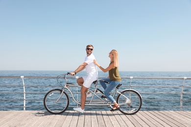Photo of Couple riding tandem bike near sea on sunny day
