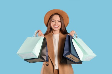 Happy young woman with shopping bags on light blue background. Big sale