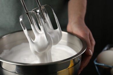 Photo of Woman making whipped cream with hand mixer on black background, closeup