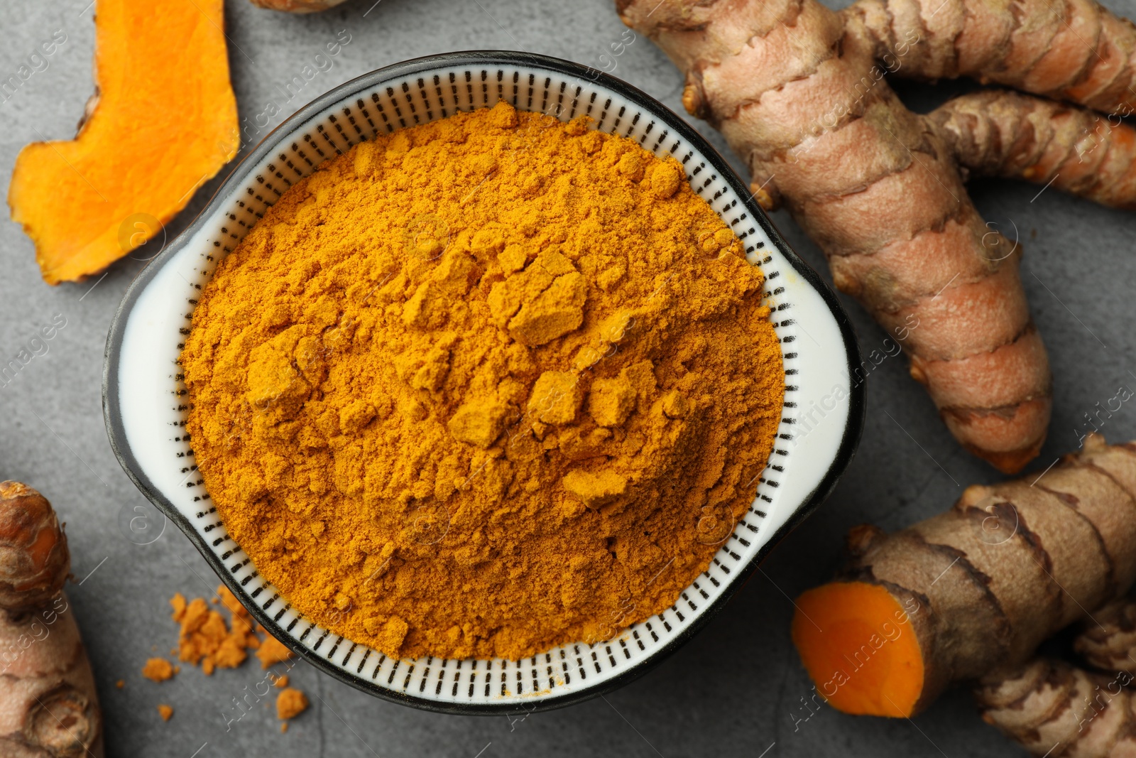 Photo of Bowl with turmeric powder and raw roots on grey table, flat lay