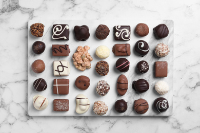 Photo of Different tasty chocolate candies on white marble table, flat lay