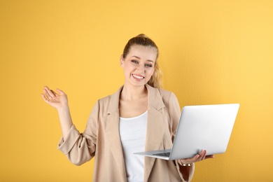 Portrait of beautiful young woman with laptop on yellow background