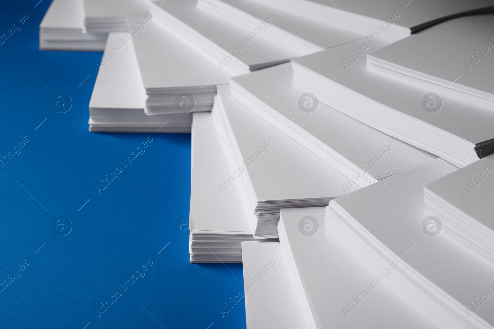 Photo of Many stacks of paper sheets on blue background, closeup