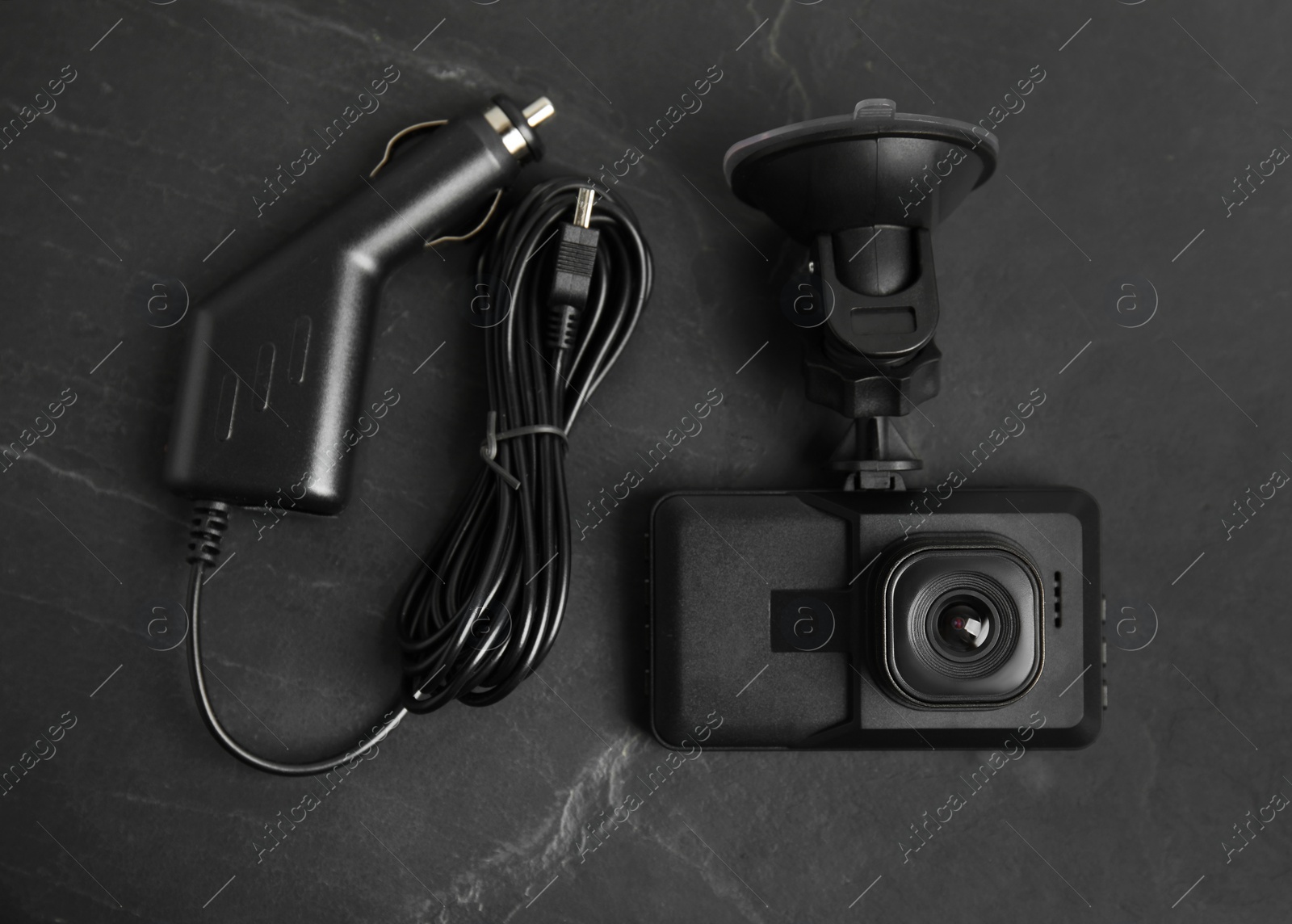 Photo of Modern car dashboard camera with suction mount and charger on black background, flat lay