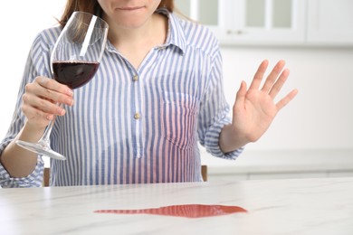 Photo of Woman with wine stain on her shirt at white marble table indoors, closeup