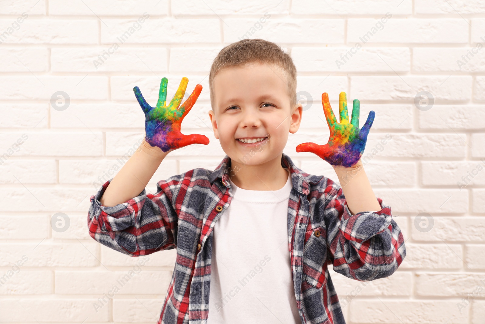 Photo of Happy little boy showing painted palms near white brick wall