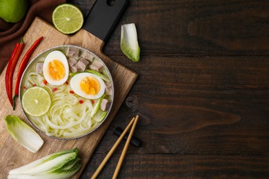 Photo of Bowl of delicious rice noodle soup with meat and egg on wooden table, flat lay. Space for text