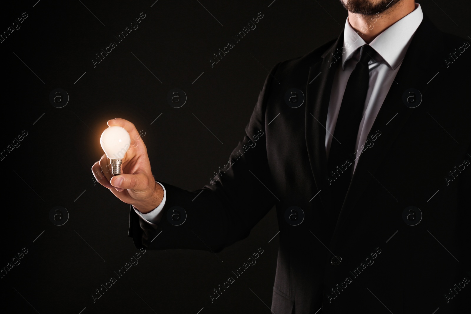 Photo of Businessman holding lamp bulb against dark background