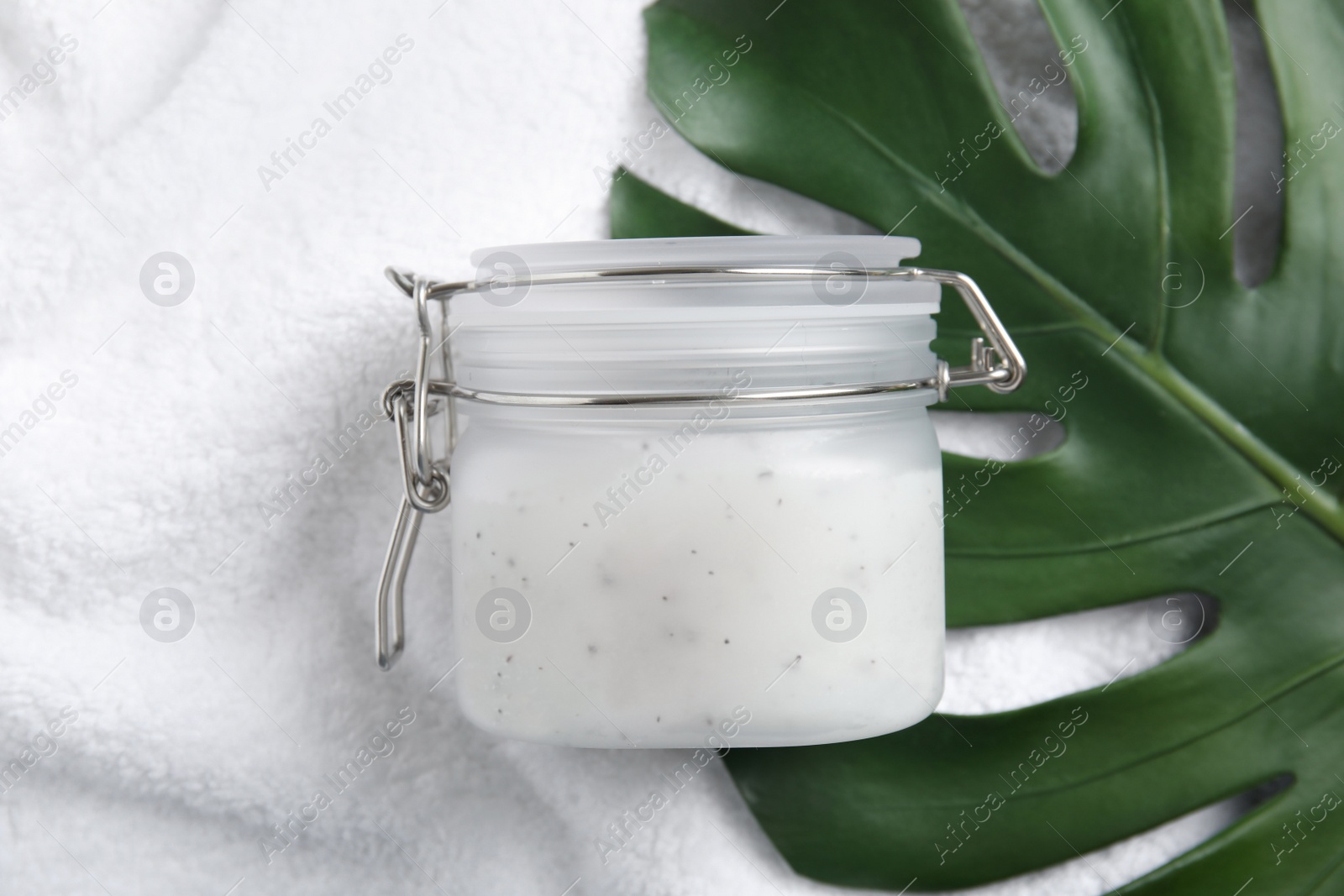 Photo of Jar of salt scrub and palm leaf on white towel, flat lay