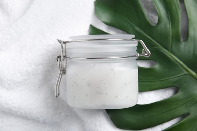 Jar of salt scrub and palm leaf on white towel, flat lay