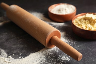 Scattered flour, rolling pin and sieve on black table, closeup