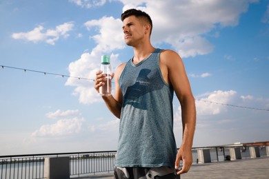 Handsome man in sportswear with bottle of water outdoors on sunny day