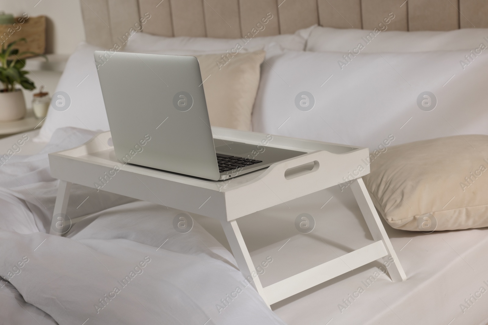 Photo of White tray table with laptop on bed indoors