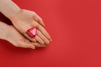 Photo of Woman holding heart shaped chocolate candy on red background, top view. Space for text