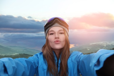 Smiling woman with ski goggles taking selfie in mountains