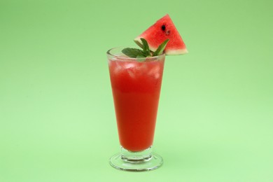 Photo of Glass of delicious drink with mint, ice cubes and cut fresh watermelon on light green background