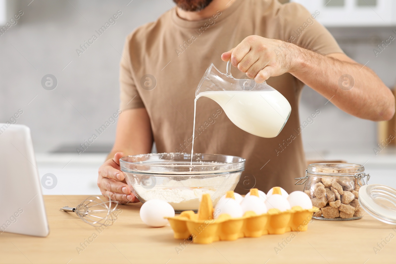 Photo of Man making dough while watching online cooking course via tablet in kitchen, closeup