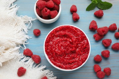 Photo of Raspberry puree in bowl and fresh berries on light blue wooden table, flat lay