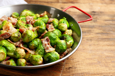Photo of Delicious Brussels sprouts with bacon on wooden table, closeup
