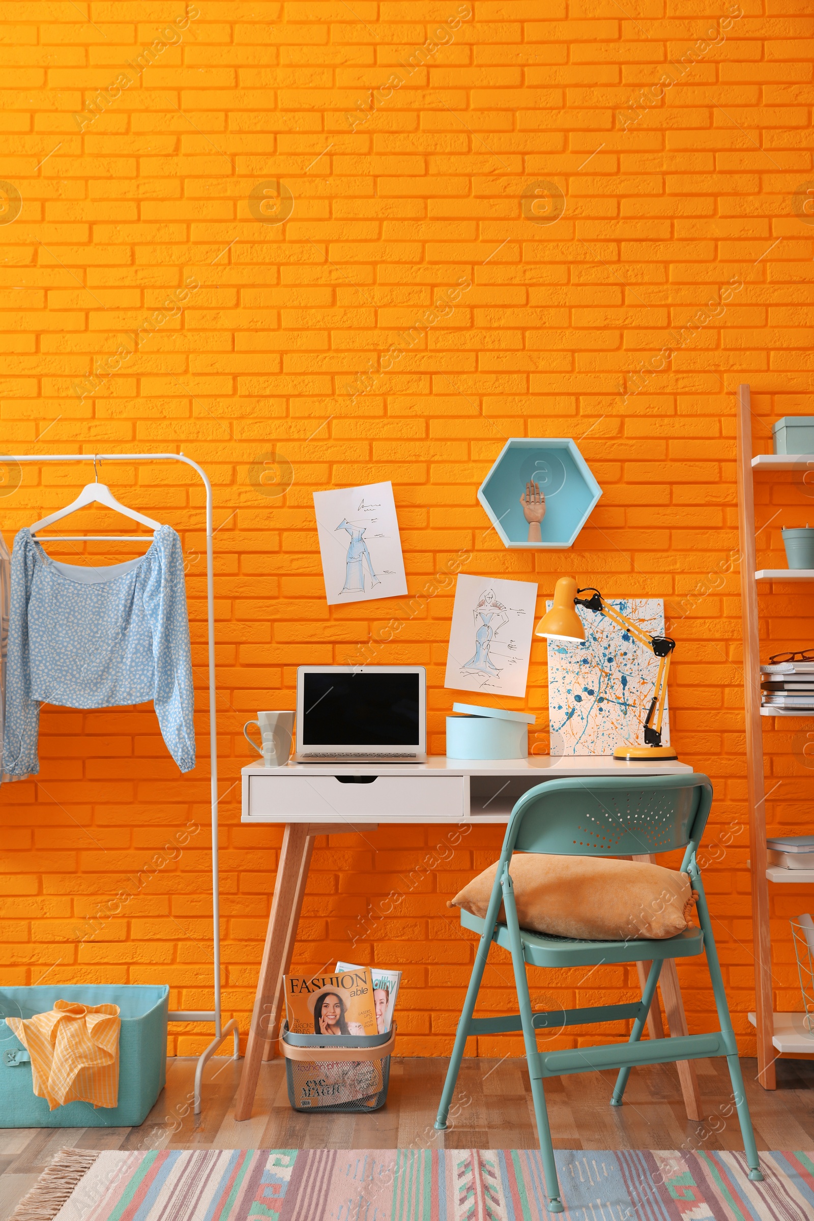 Image of Fashion designer's workplace with wooden furniture and laptop near orange brick wall. Stylish interior