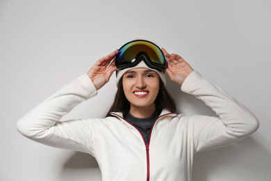 Photo of Woman wearing fleece jacket and goggles on light grey background. Winter sport clothes