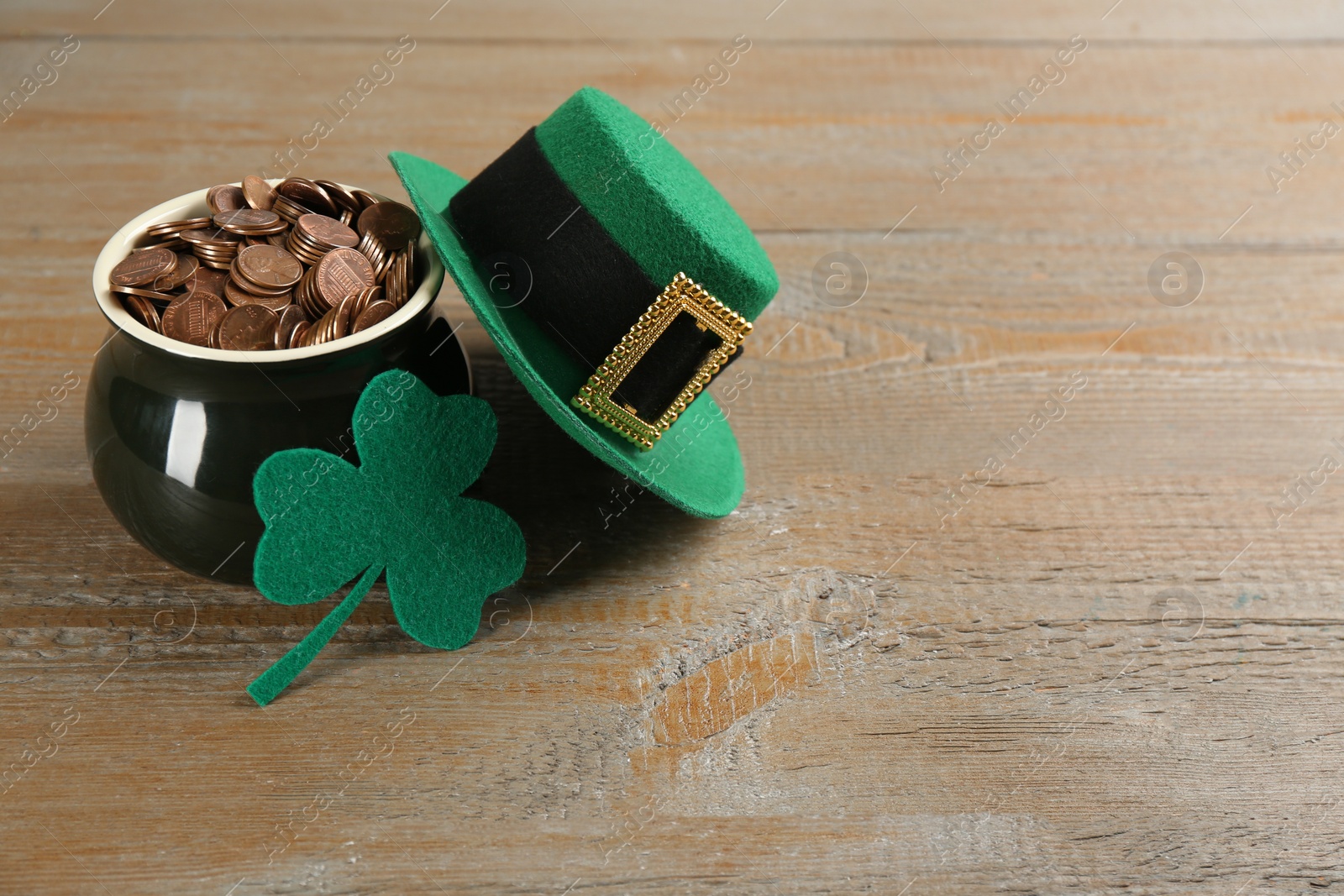 Photo of Pot of gold coins, hat and felt clover leaf on wooden table, space for text. St. Patrick's Day celebration