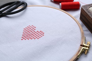 Photo of Embroidered red heart and scissors on white cloth, closeup