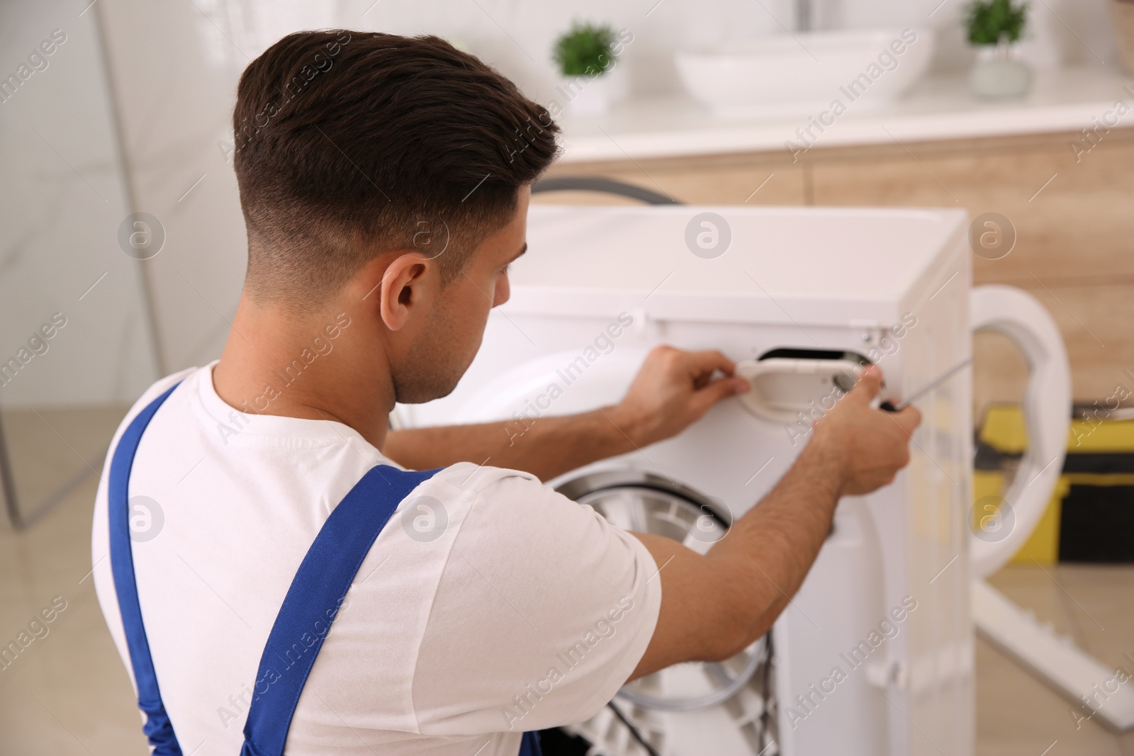 Photo of Professional plumber repairing washing machine in bathroom