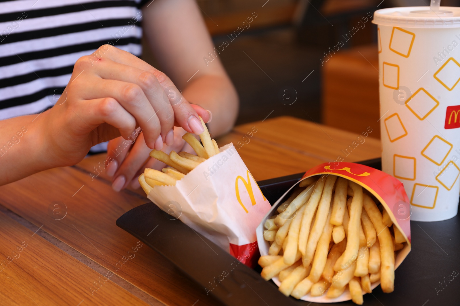 Photo of MYKOLAIV, UKRAINE - AUGUST 11, 2021: Woman with McDonald's French fries and drink at table in cafe, closeup