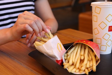 Photo of MYKOLAIV, UKRAINE - AUGUST 11, 2021: Woman with McDonald's French fries and drink at table in cafe, closeup