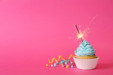 Photo of Birthday cupcake with burning sparkler and streamers on pink background. Space for text
