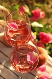 Photo of Glasses of delicious rose wine with petals on white picnic blanket outside, above view