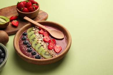 Bowl of delicious smoothie with fresh blueberries, strawberries, kiwi slices and oatmeal on light green background. Space for text