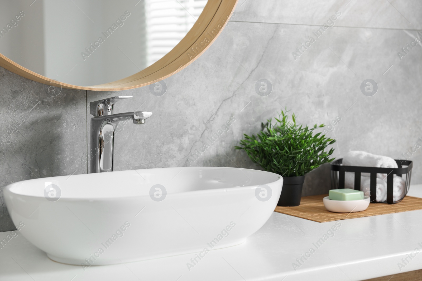 Photo of Potted artificial plants, rolled towels and soap near sink on bathroom vanity