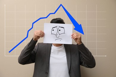 Image of Businessman holding card with drawn frowning face and illustration of falling down chart on beige background. Economy recession concept