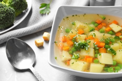 Bowl of fresh homemade vegetable soup served on grey marble table, closeup