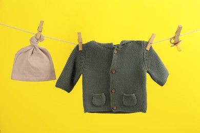 Baby clothes and accessories hanging on washing line against yellow background